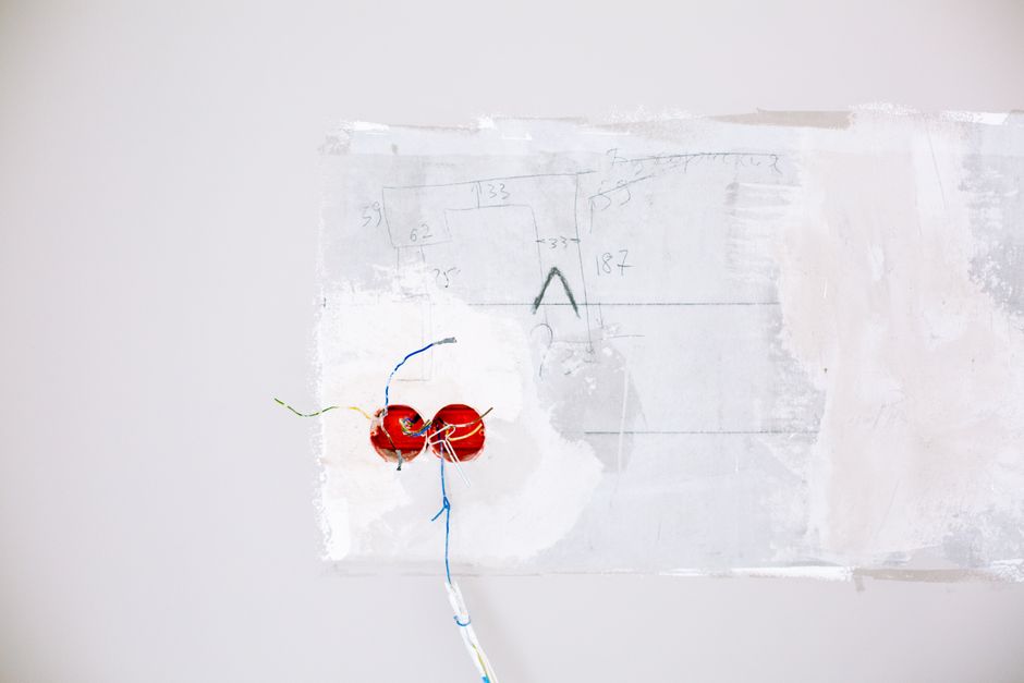 Close-up view of exposed electric wiring being installed during home renovation on a white wall.