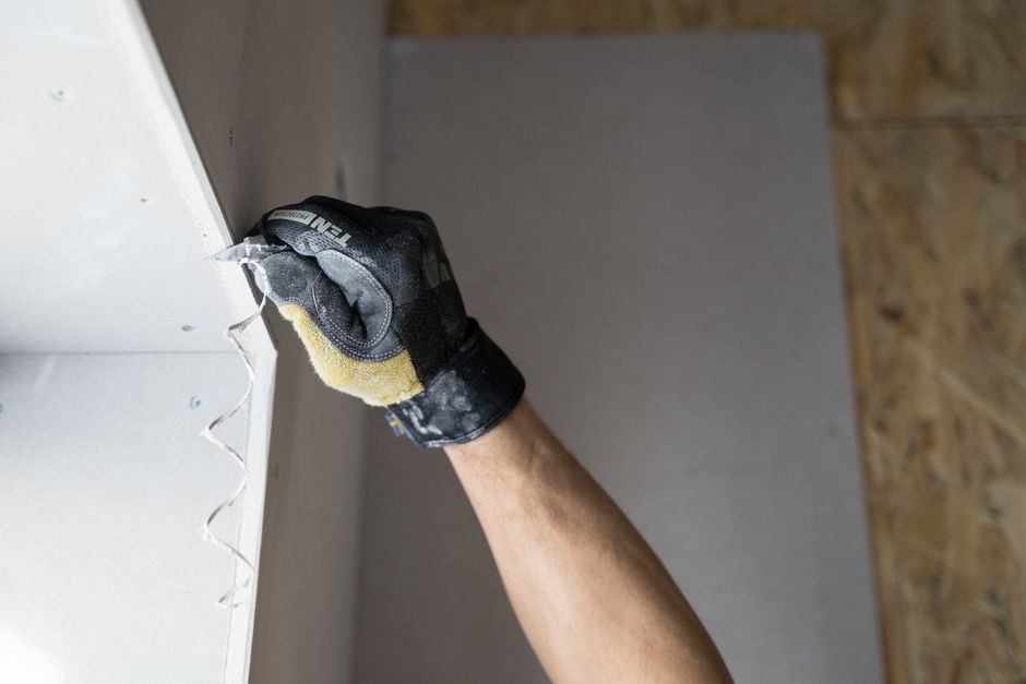 Close-up of a gloved hand applying plaster to a wall.