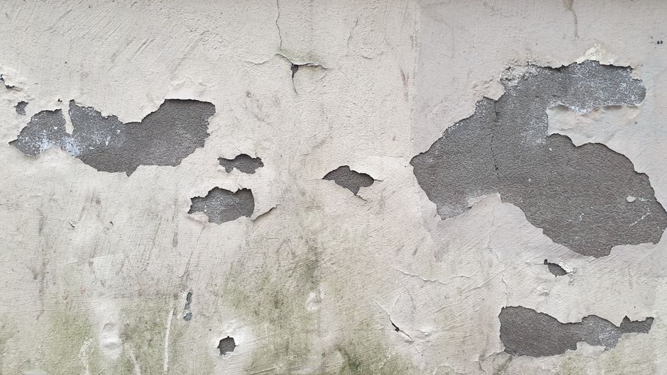 Close-up of an aged concrete wall with peeling paint and cracked surface, rich in texture.